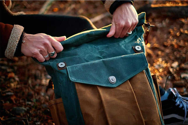 Hands closing the top of a green Lund canvas backpack