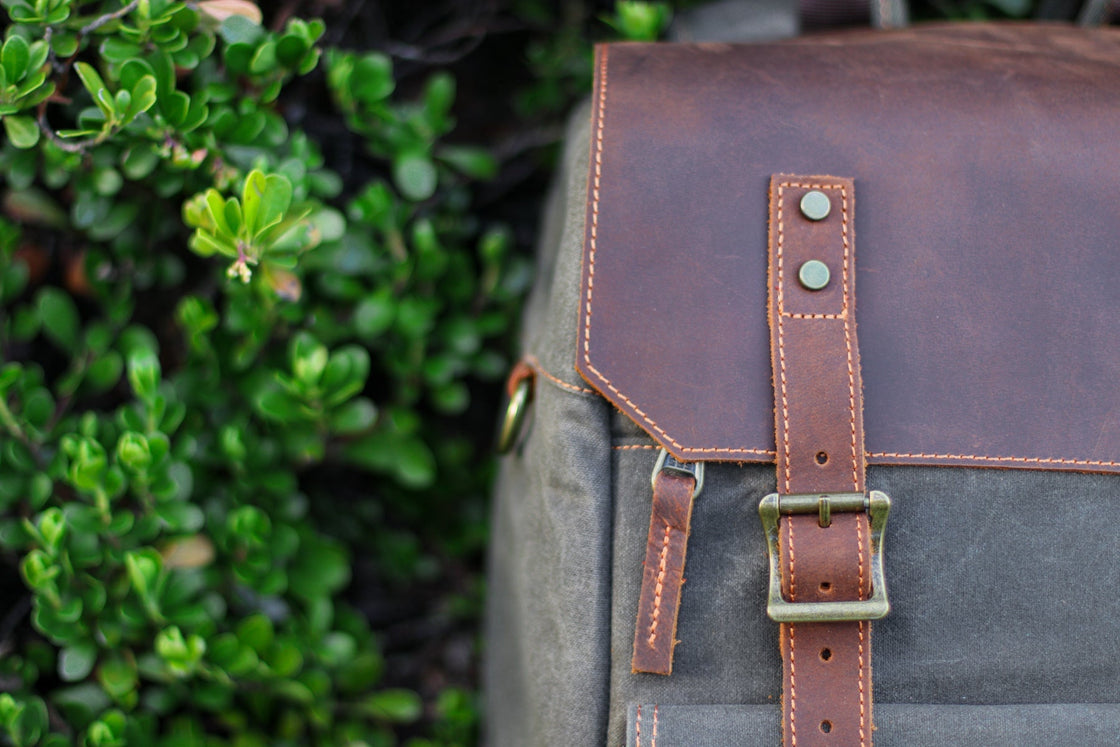Macro of the antiqued brass square buckle and full-grain leather strap with orange topstitching on the Algonquin flap closure