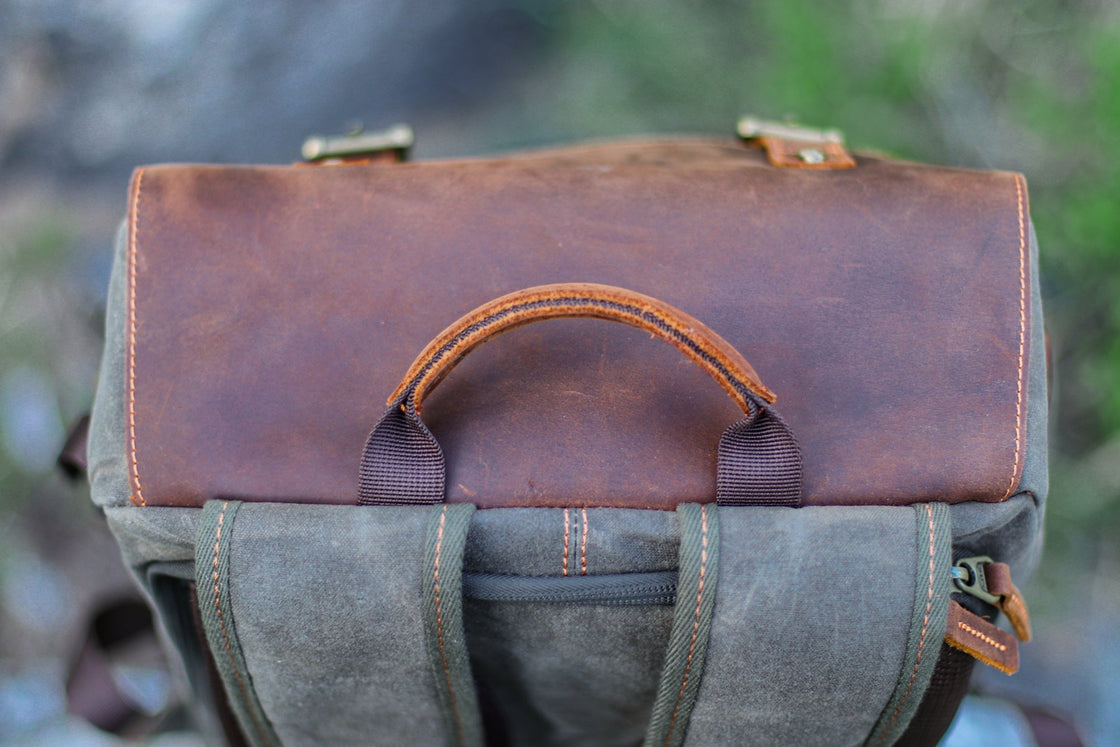 Top-down close-up of the cotton-wrapped leather grab handle on the Algonquin flap, with reinforced webbing keepers and orange topstitching