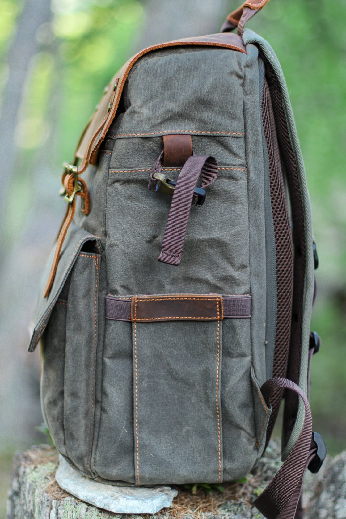 Profil latéral du sac à dos photographe Algonquin vert gris foncé sur une souche d'arbre, montrant la profondeur, le dos en mesh ventilé et les sangles de compression latérales