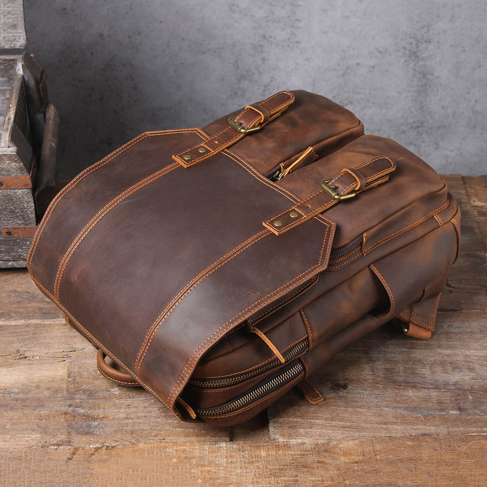 brown leather rucksack lying flat, flap folded back over the buckle straps