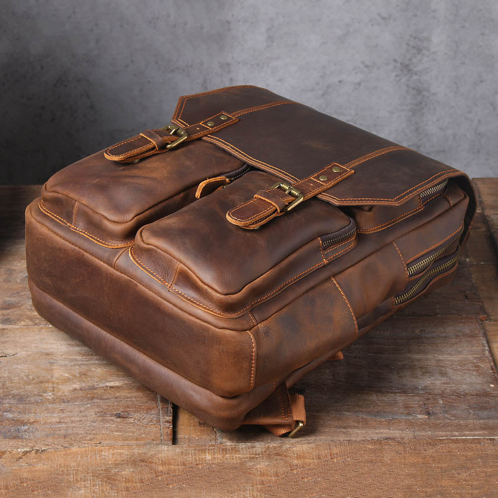 brown leather rucksack lying on its back on a wooden table, front pockets uppermost