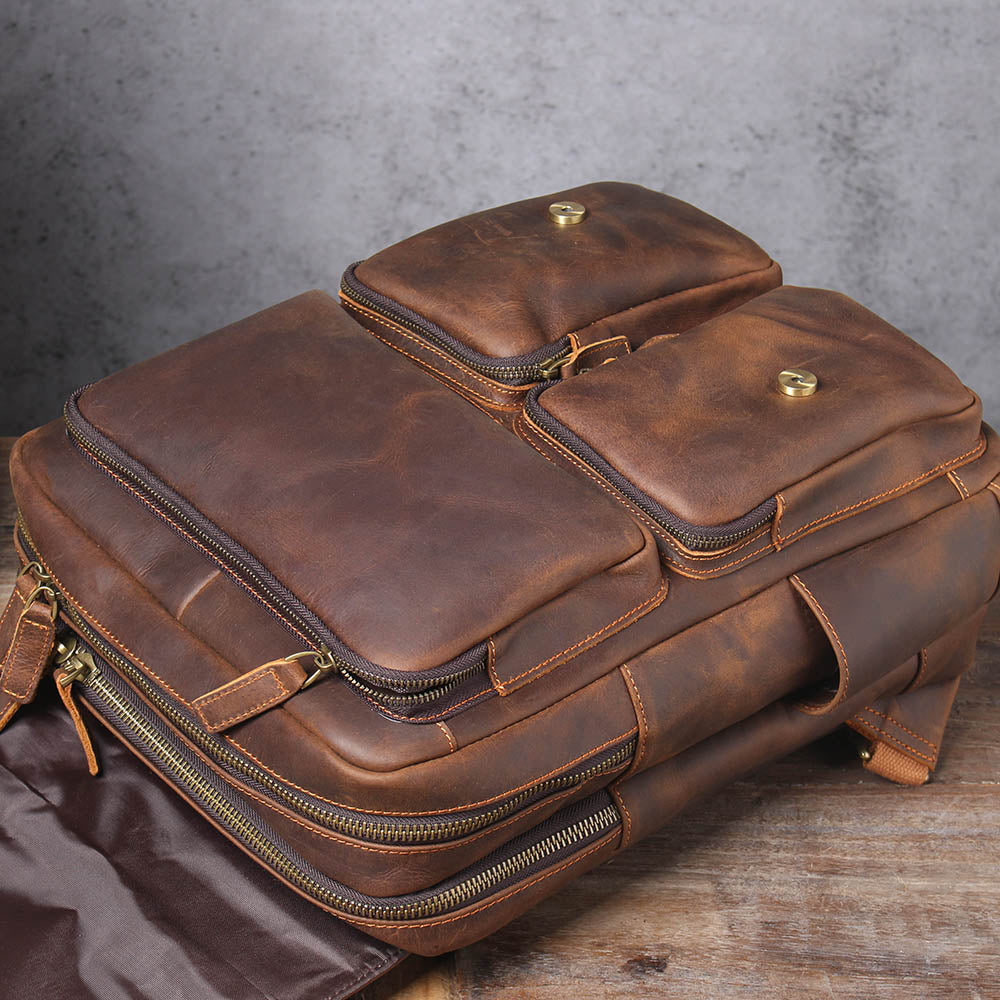 top of the brown leather rucksack with the flap raised, main zip and front pockets in view