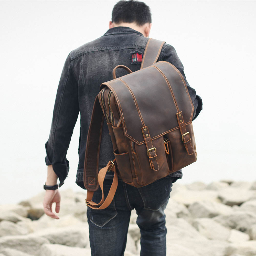 man walking away with the brown leather rucksack on his back by the sea