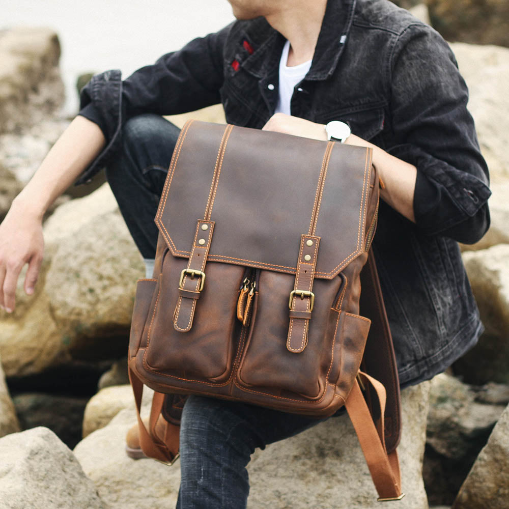 man seated on rocks holding the brown leather rucksack on his knees
