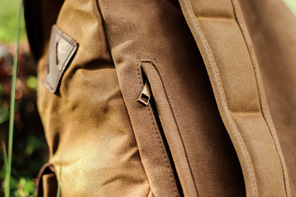 Close-up of the side hidden YKK zipper pocket with brass-edged opening on the khaki Calgary canvas backpack