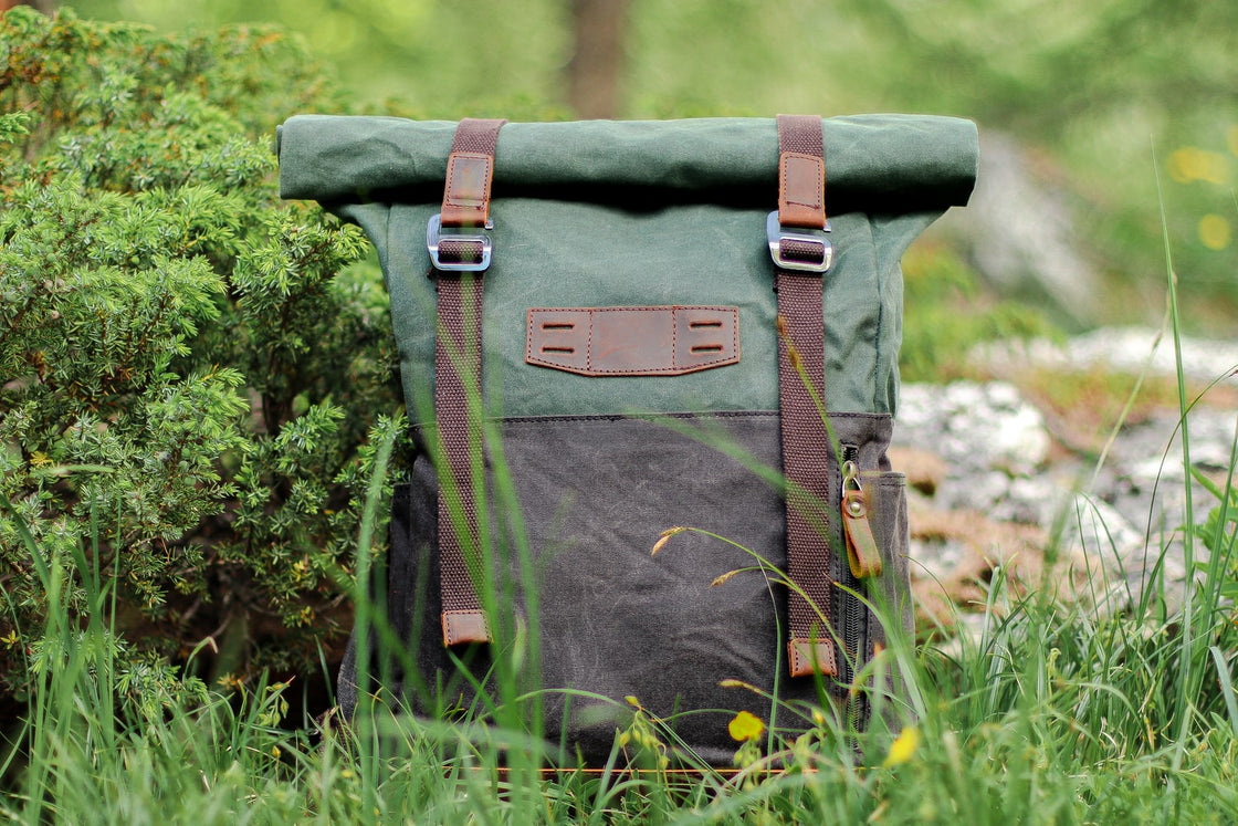 Sac à dos urbain Dublin kaki en toile dans l'herbe alpine près de genévrier, rabat en cuir captant la lumière