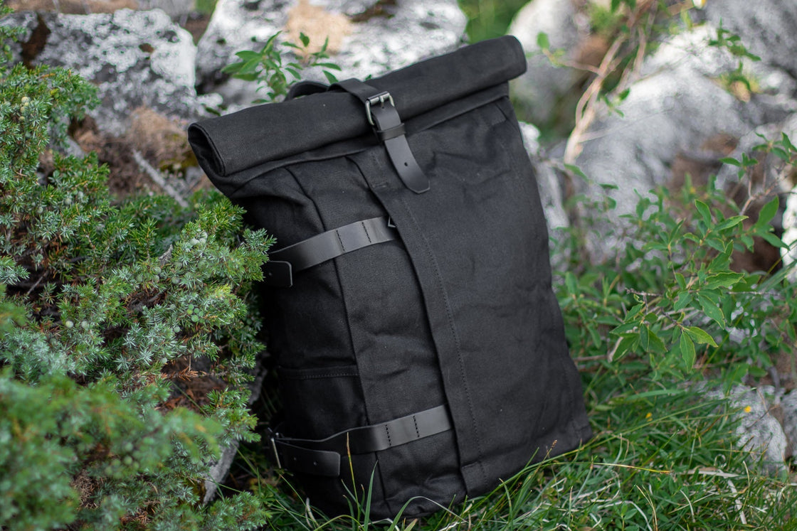 Gstaad noir en sac motard pour casque ou selle photographié de trois-quarts sur l'herbe entre rochers forestiers