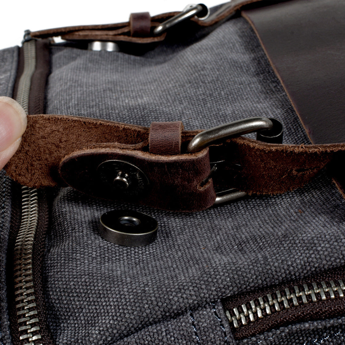 Macro of the magnetic snap clip and full-grain leather strap closure on the Milan dark grey canvas backpack