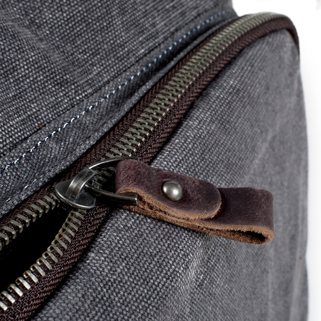 Macro detail of the zipper with full-grain leather pull tab and brass D-ring on the side of the Milan dark grey canvas backpack