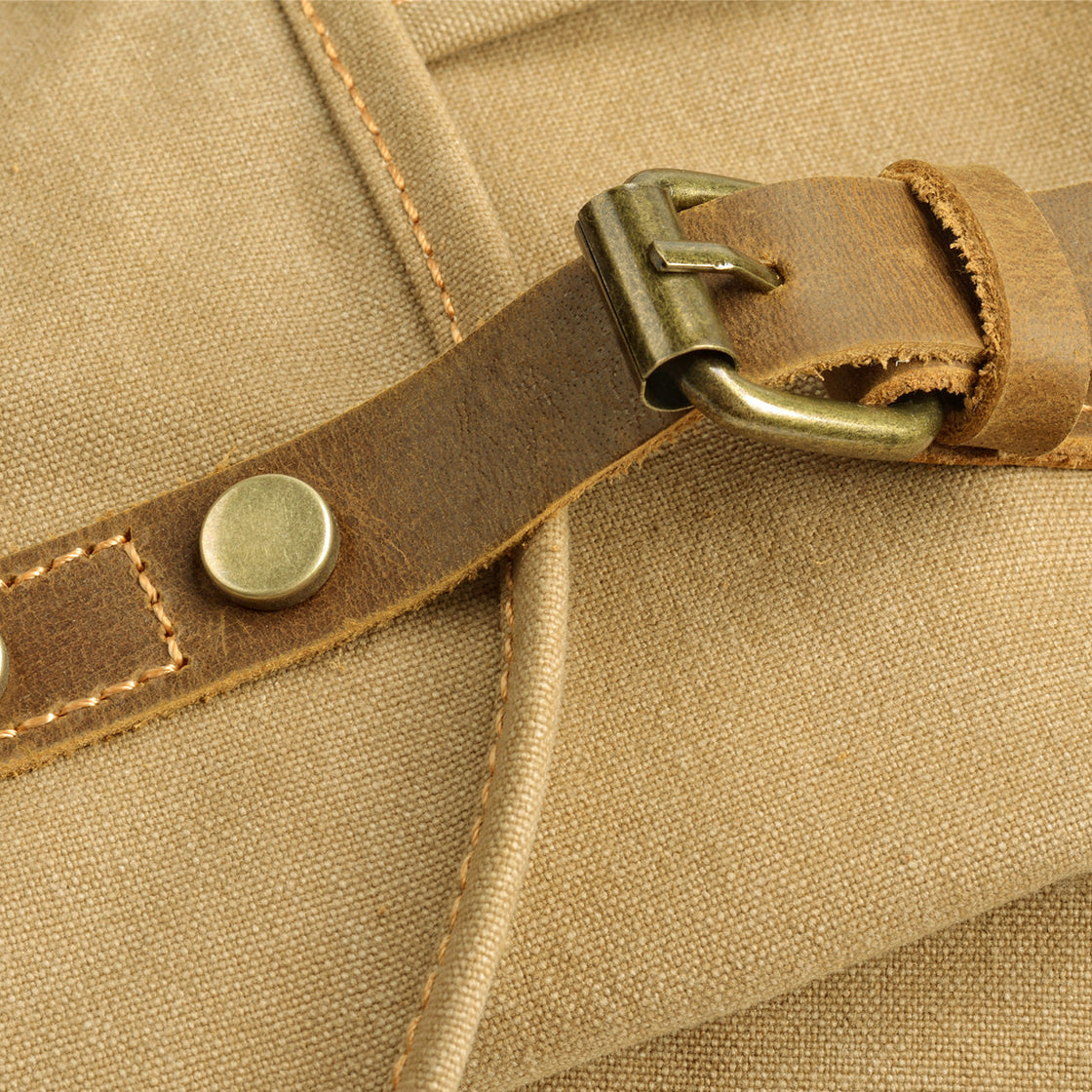 Macro of the antiqued brass roller buckle and full-grain leather strap with brass rivet on the khaki Montreal canvas body