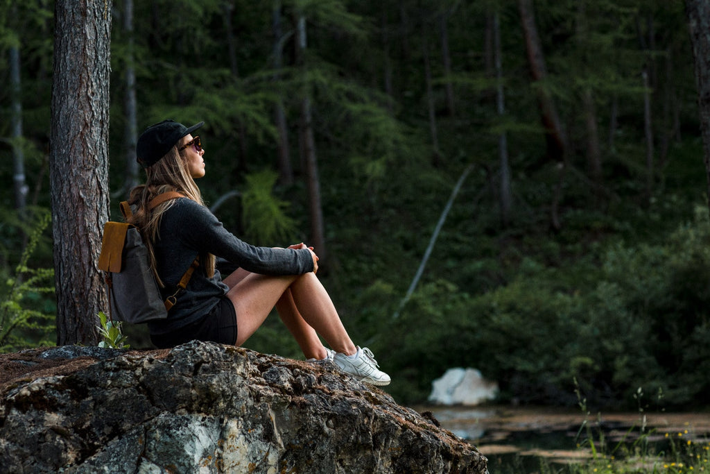 Front view of the charcoal grey Nora women's canvas backpack on a wooden bench, leather flap with magnetic snap closure