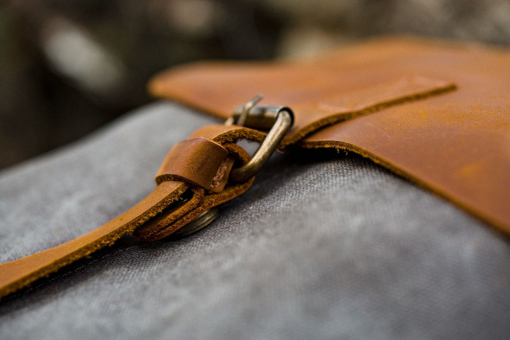 Macro detail of the leather flap with brass magnetic snap on the Nora women's canvas backpack