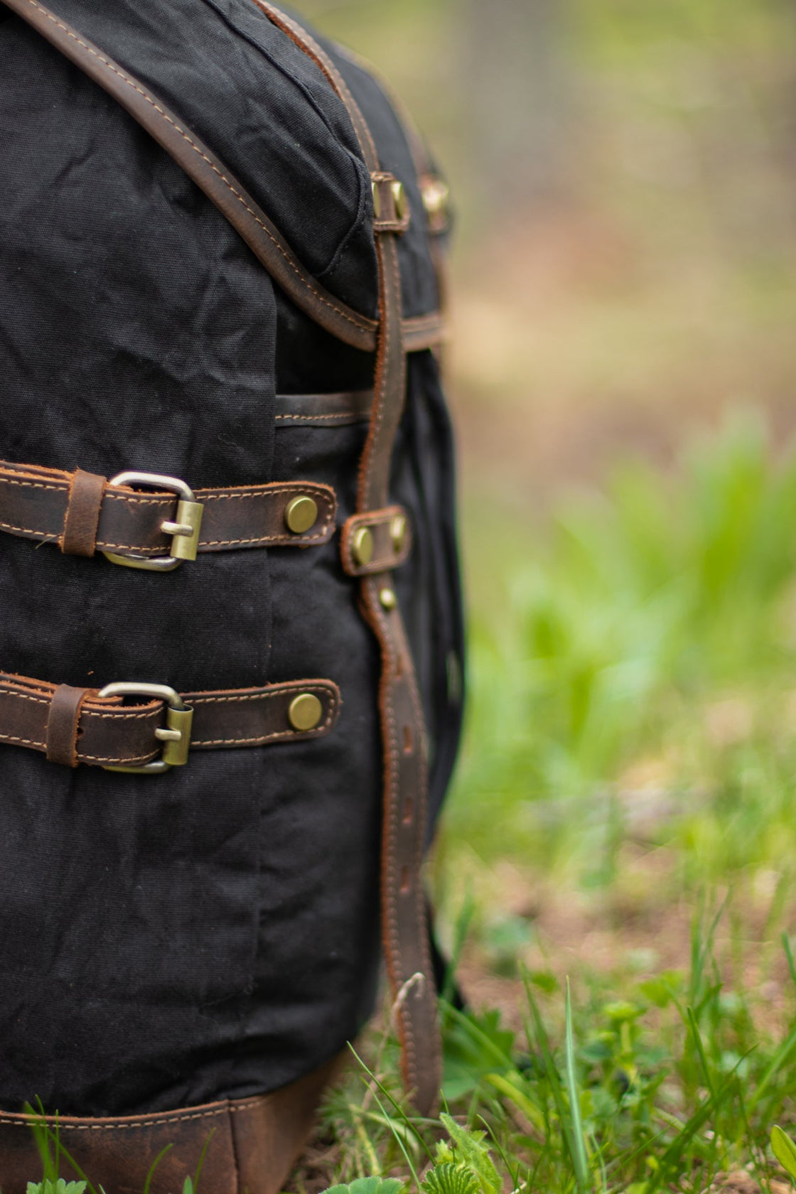 Macro des doubles sangles cuir latérales noires avec boucles laiton antique et coutures contrastes sur le Rostock en milieu forestier