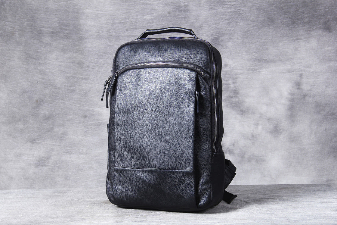 black leather laptop backpack held upright in both hands, pebbled cowhide and gunmetal zips