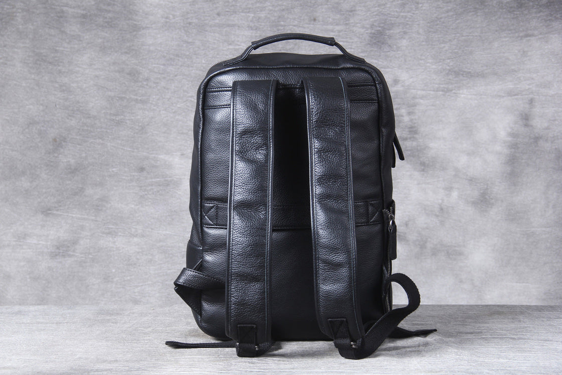 sliding a laptop into the top zip of the black leather backpack while seated