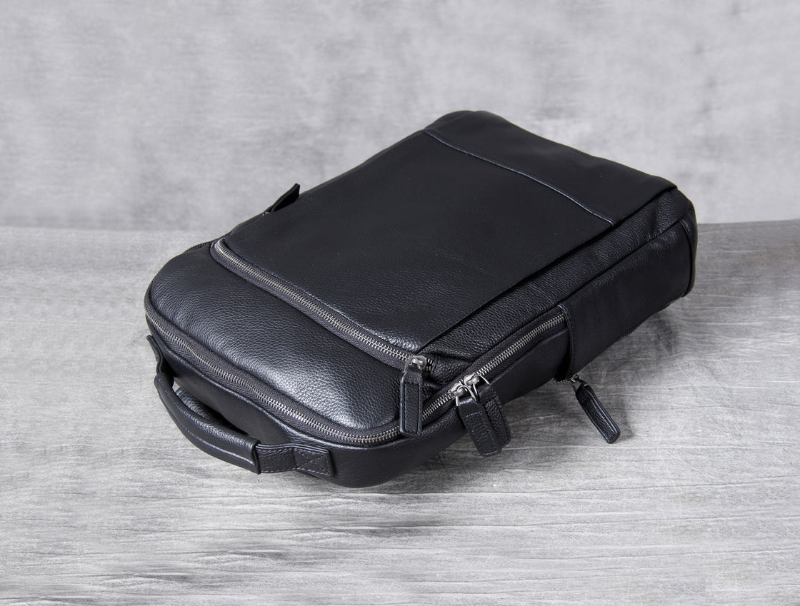 black leather laptop backpack lying on grey boards, twin main zips in the foreground