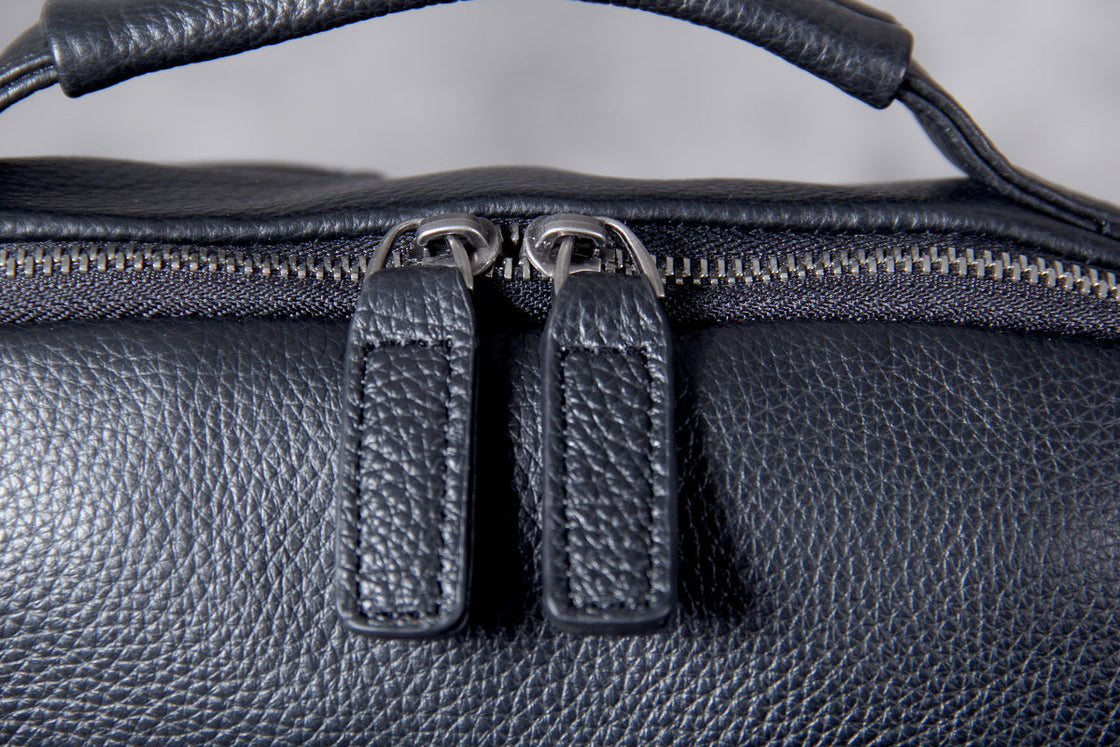 twin gunmetal zip pulls with pebbled leather tabs on the main compartment