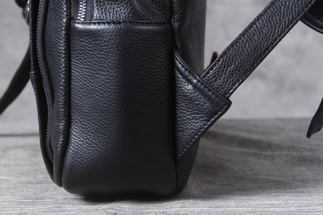leather laptop backpack packed with a phone, a bottle, a wallet and a laptop under the retaining strap