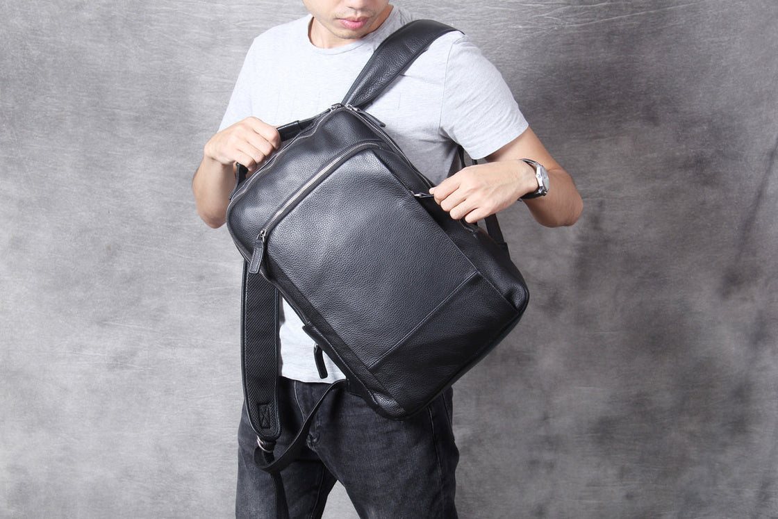 man opening the vertical front zip pocket of the black leather backpack