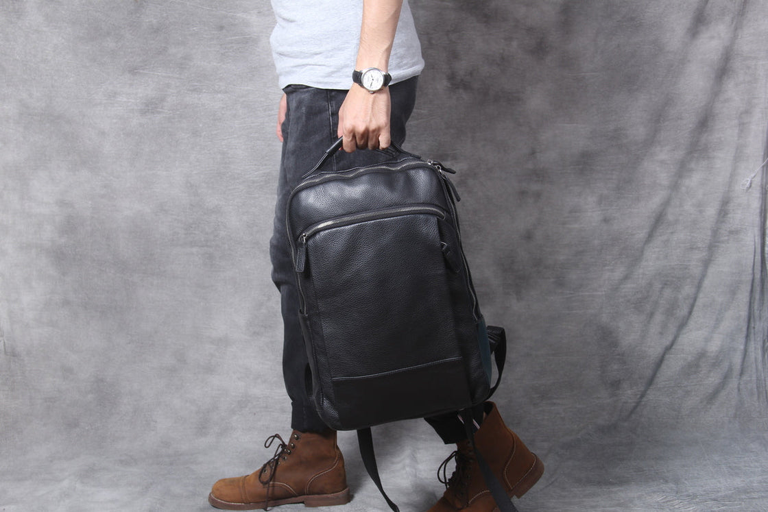 man holding the black leather laptop backpack by its leather top handle