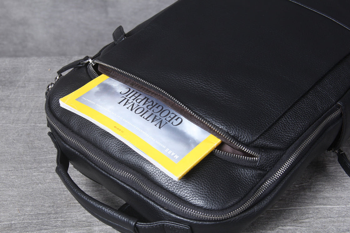 black leather laptop backpack lying flat, top handle and gunmetal zips from above