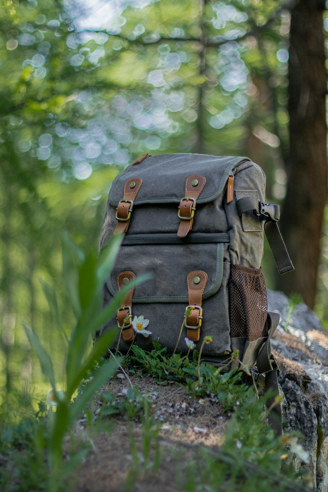 Army green Vilnius waxed canvas camera backpack photographed on a forest rock with side mesh pocket visible