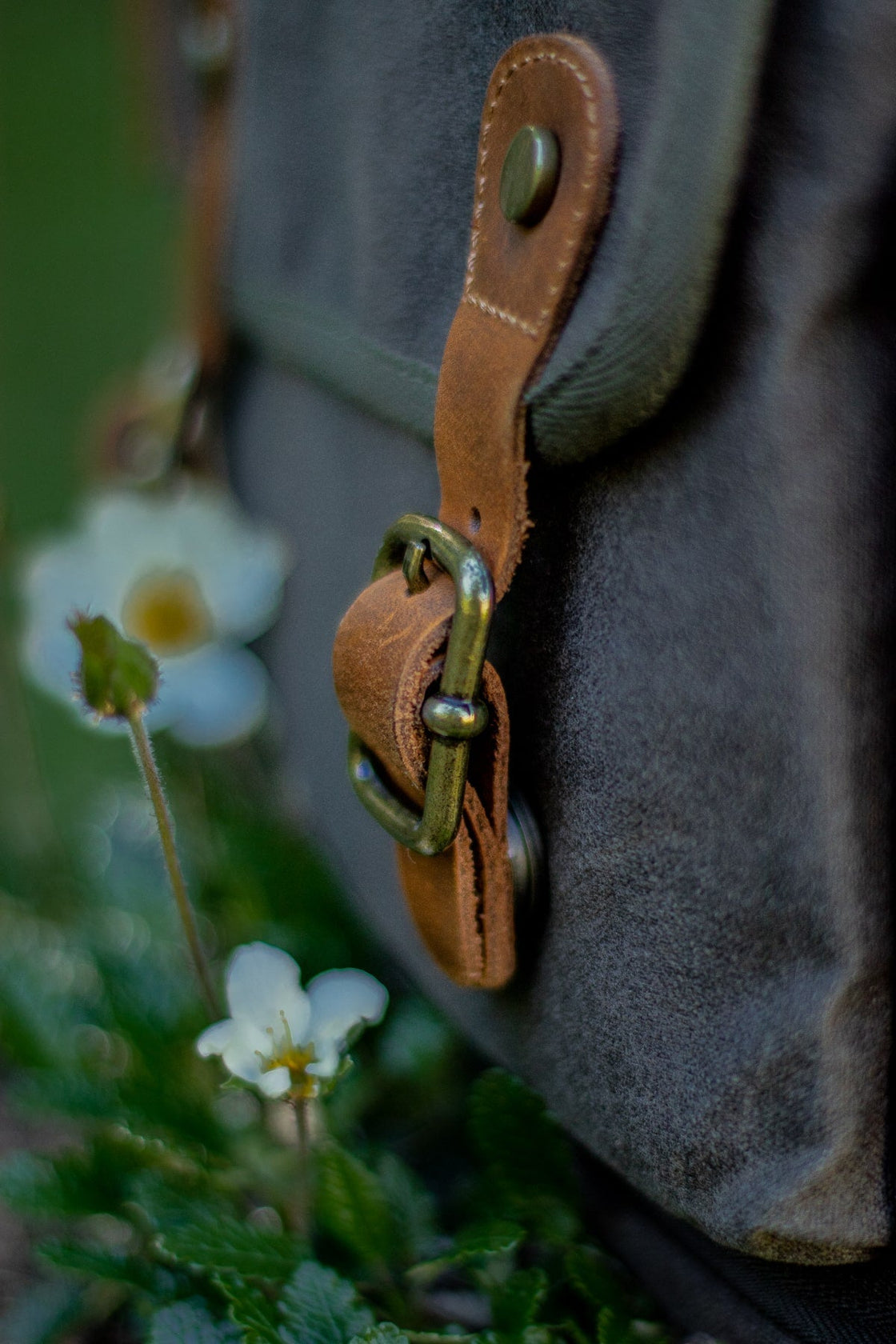 Macro de l'anneau laiton et passant cuir sur le Vilnius vert kaki entouré de fleurs sauvages