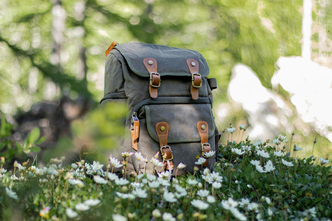 Petit sac photo Vilnius vert kaki dans une prairie de fleurs sauvages, sangles cuir et bretelles visibles