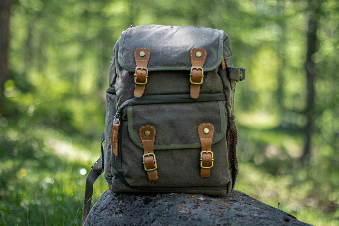 Sac à dos appareil photo vert kaki photographié sur un rocher en forêt avec doubles boucles cuir, poche frontale et poche filet, DIYION Vilnius