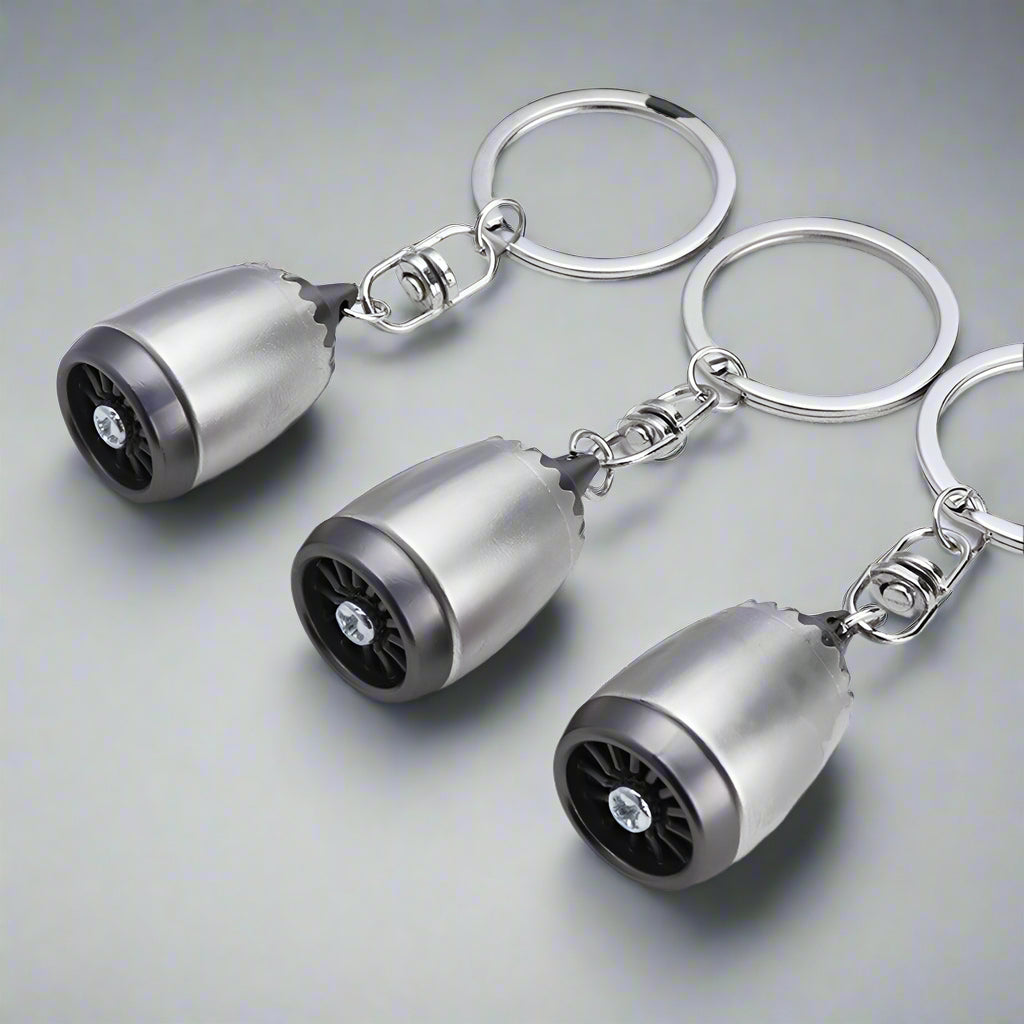 Three metallic keychains shaped like small turbines on a gray background