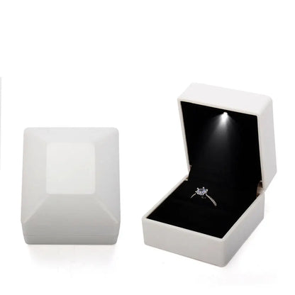 Open white jewelry box with a black interior containing a diamond ring on a LED ring box with automatic light for engagement proposals and wedding jewelry display