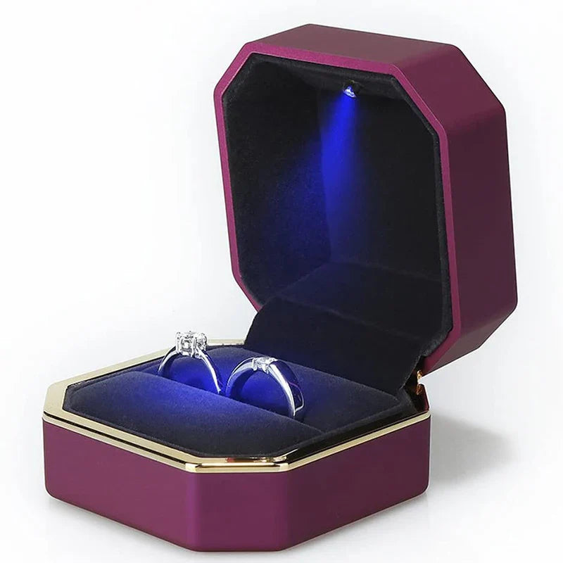 Purple jewelry box with a blue interior containing a ring, illuminated from within. LED ring box with automatic light for engagement proposals and wedding jewelry display