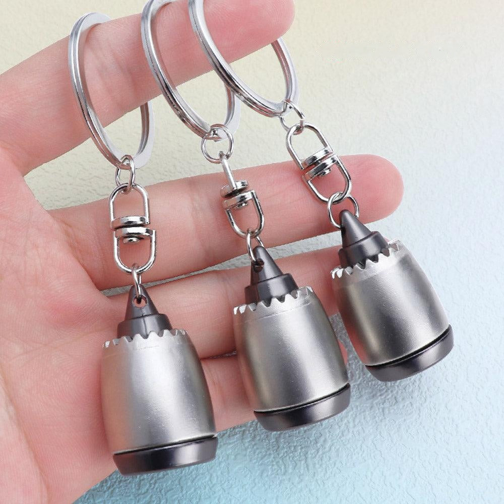Three metallic drill bit keychains held in a hand against a light blue background